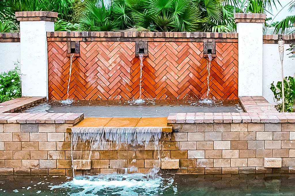 A water fountain in a backyard with palm trees.